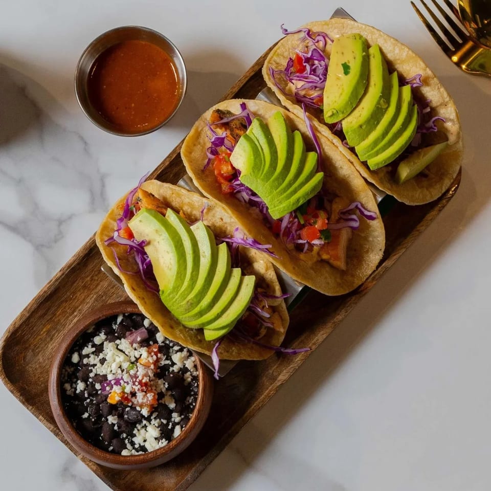 Three Kairos Jax tacos with avocado, red cabbage, and salsa, served with black beans.