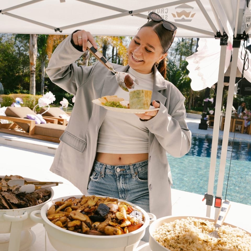A smiling woman serves herself healthy food from a buffet next to a pool at Kairos Jax.