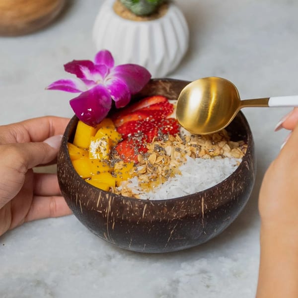 Hands holding a Kairos Jax acai bowl with mango, strawberries, granola, and coconut flakes.