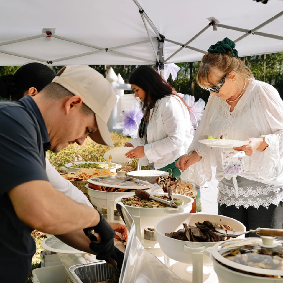 People serving themselves healthy food from a buffet line under a white tent at Kairos Jax.