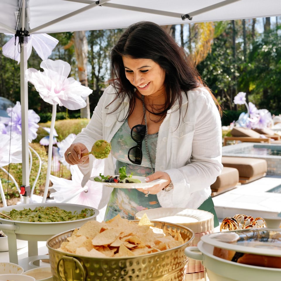 A smiling woman serves herself a healthy salad and guacamole at an outdoor event.
